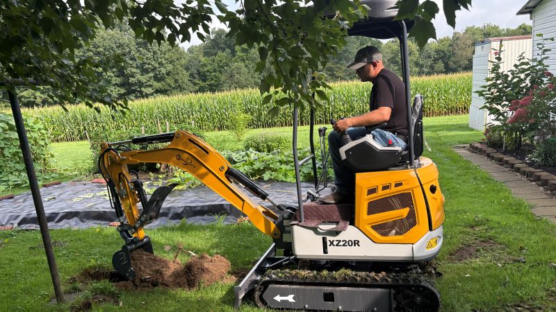Mini excavator digging in a back yard beside a tree